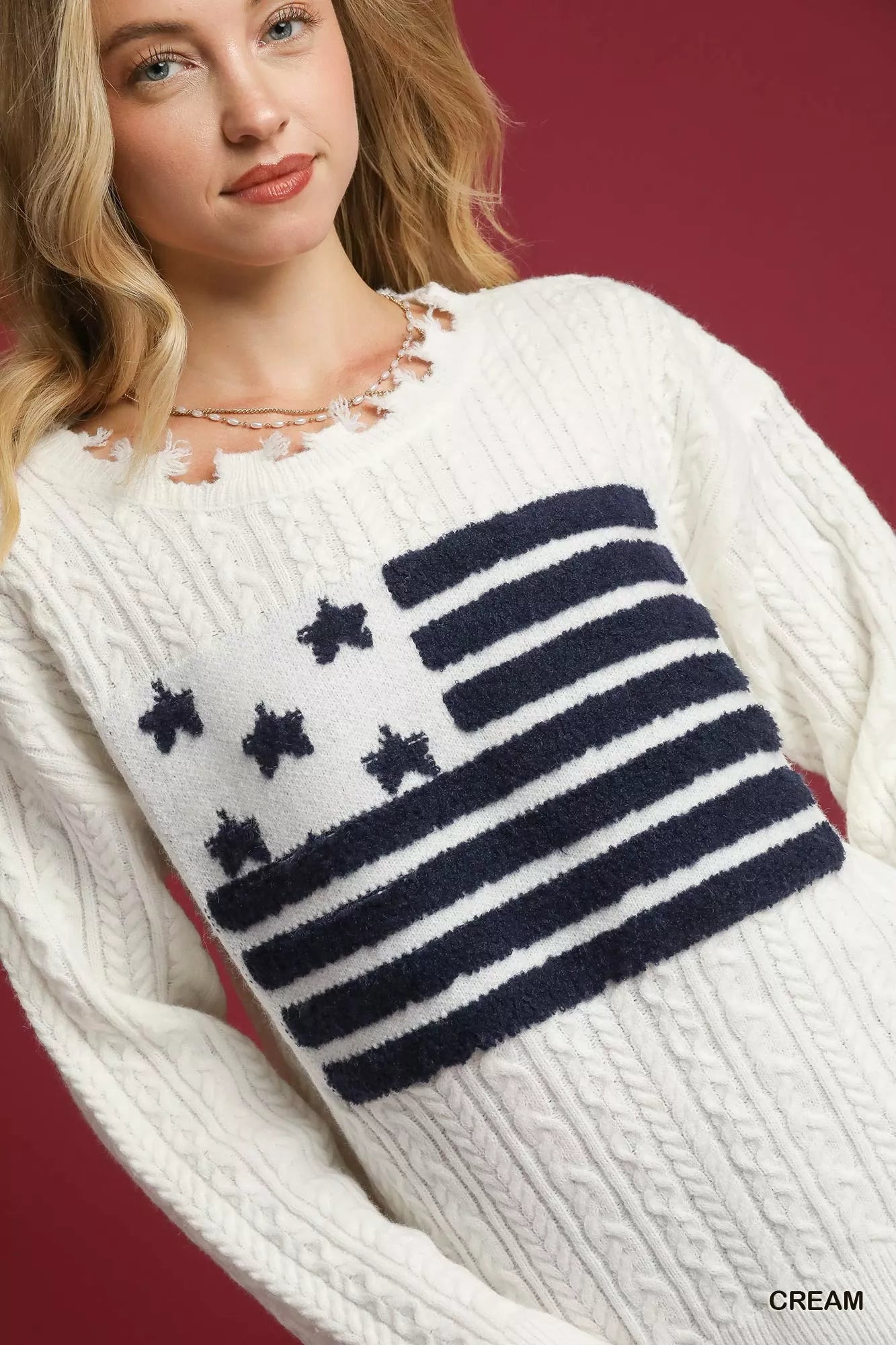Woman wearing cream distressed American flag sweater with raw hem and vintage design