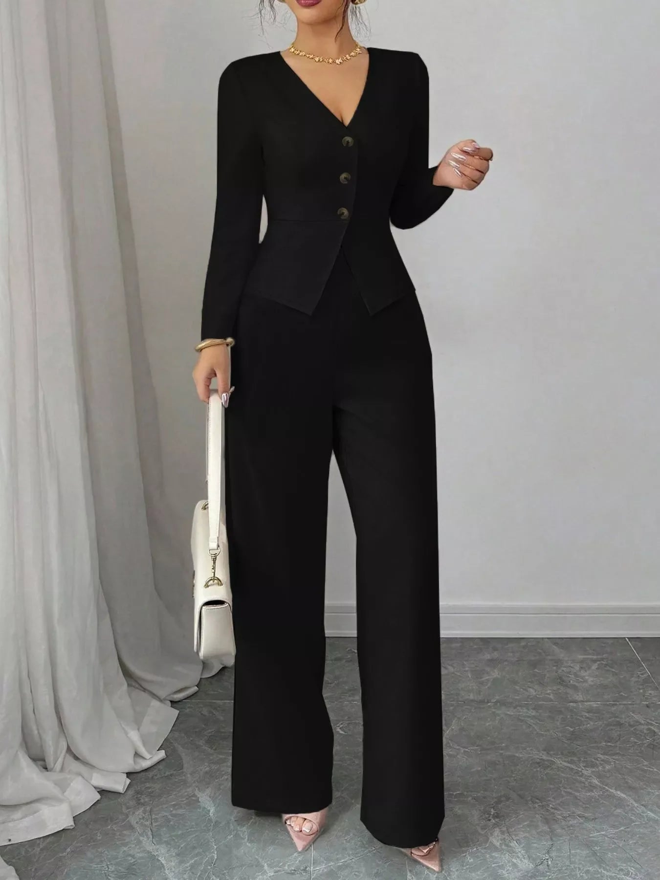Woman wearing black button up long sleeve top and pants set with long sleeves and tailored fit, holding white handbag and wearing pointed heels