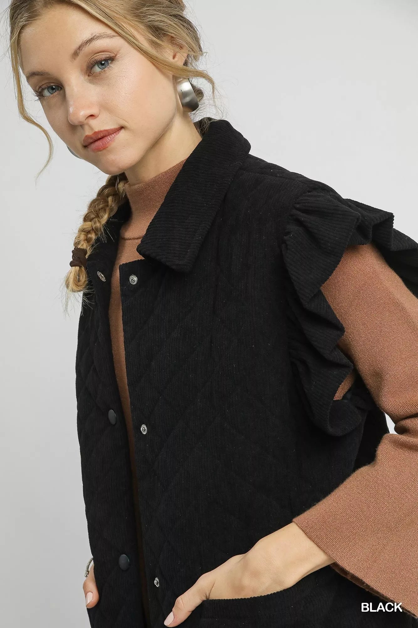 Woman wearing black Umgee Corduroy Quilted Ruffle Sleeve Vest with button closure and ruffle cap sleeves over brown long sleeve top