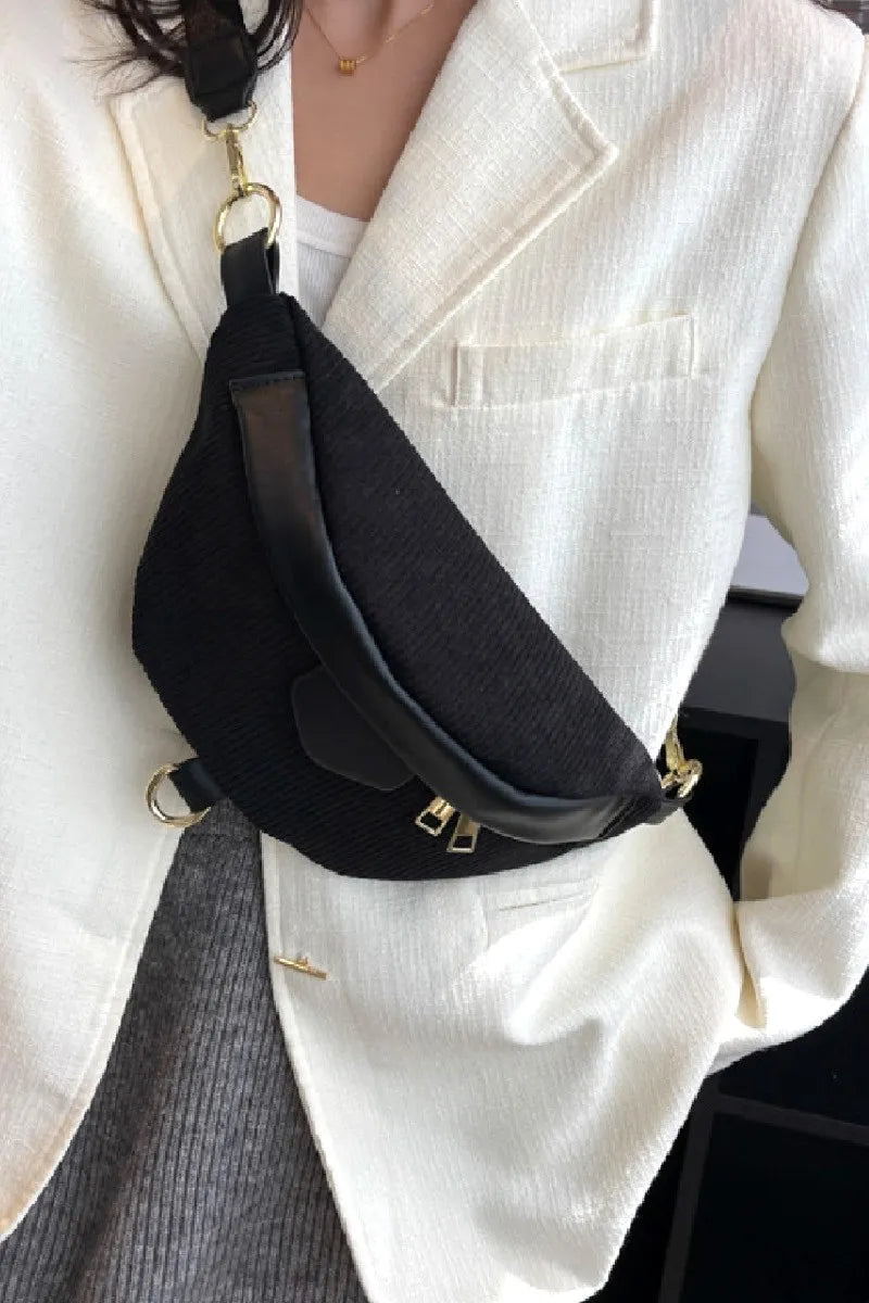 Black corduroy crossbody bag with removable strap worn over white blazer