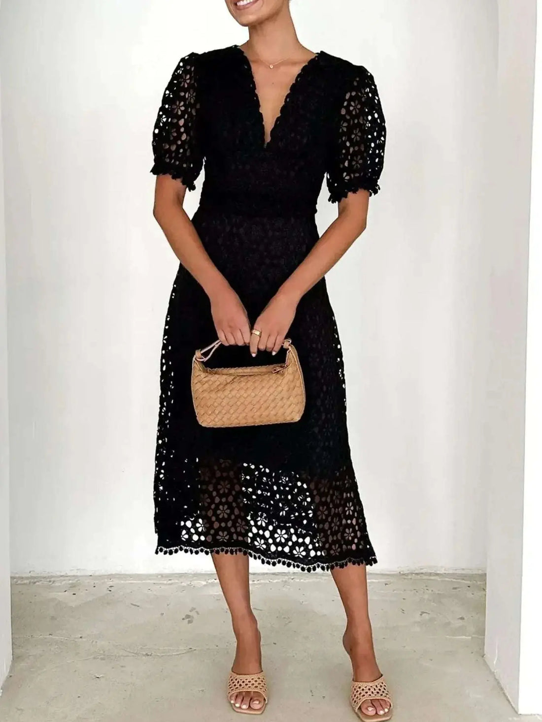 Woman wearing a black lace midi dress with short puff sleeves, holding a beige woven handbag, styled for versatile wardrobe organization tips.