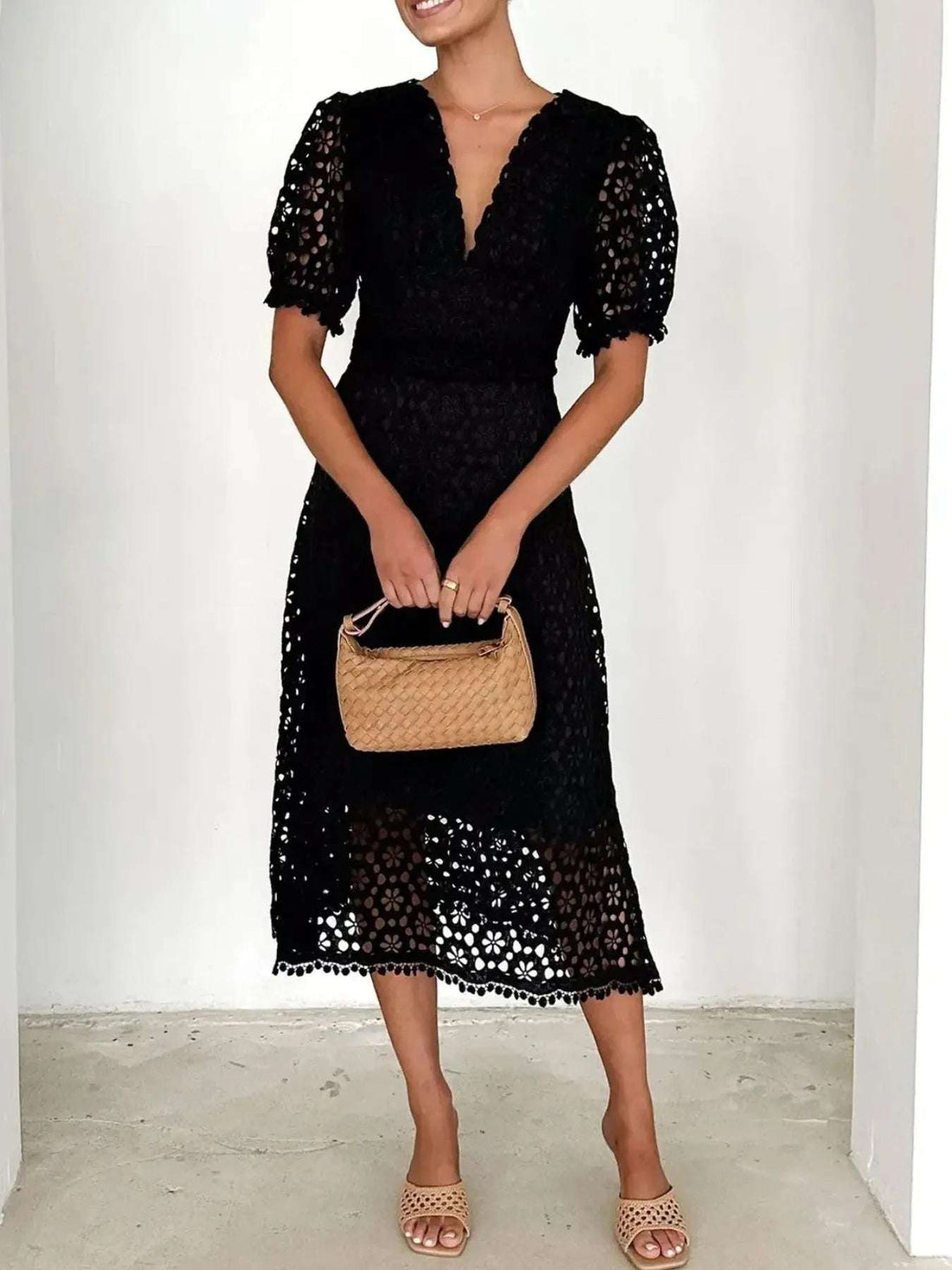 Woman wearing a black lace midi dress with short puff sleeves, holding a beige woven handbag, styled for versatile wardrobe organization tips.
