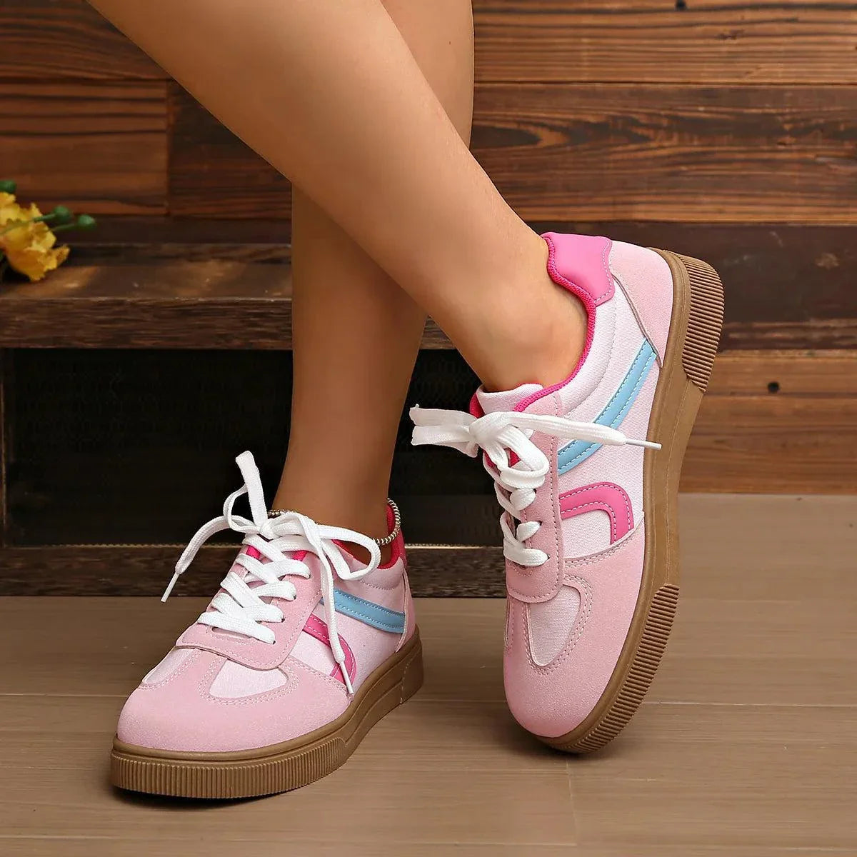 Pink lace up platform sneakers with white laces, blue and pink accents, and brown rubber soles worn on feet indoors.
