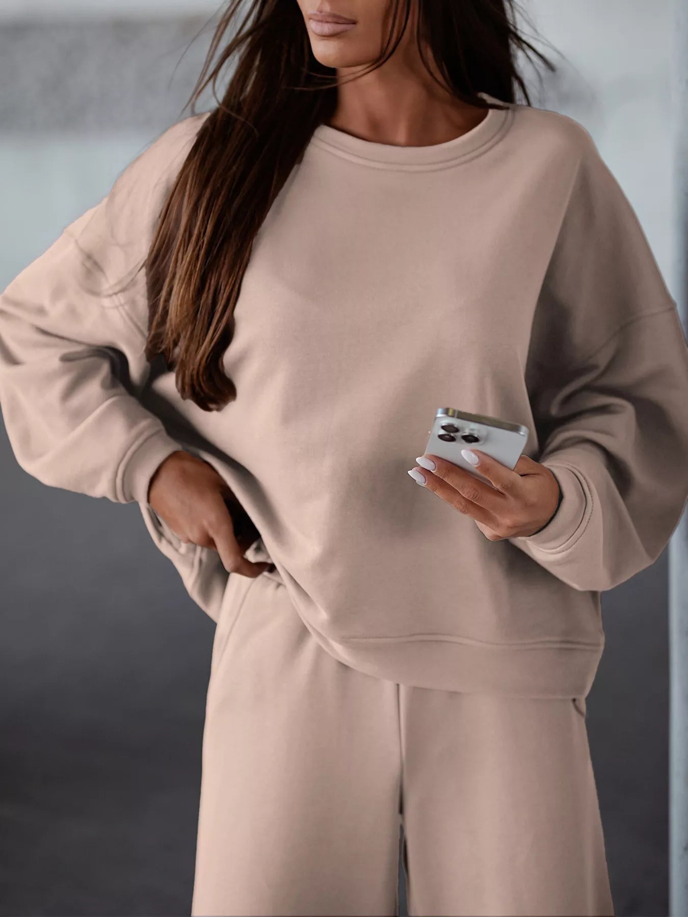 Woman wearing beige casual loose fit top and pants two-piece set holding smartphone