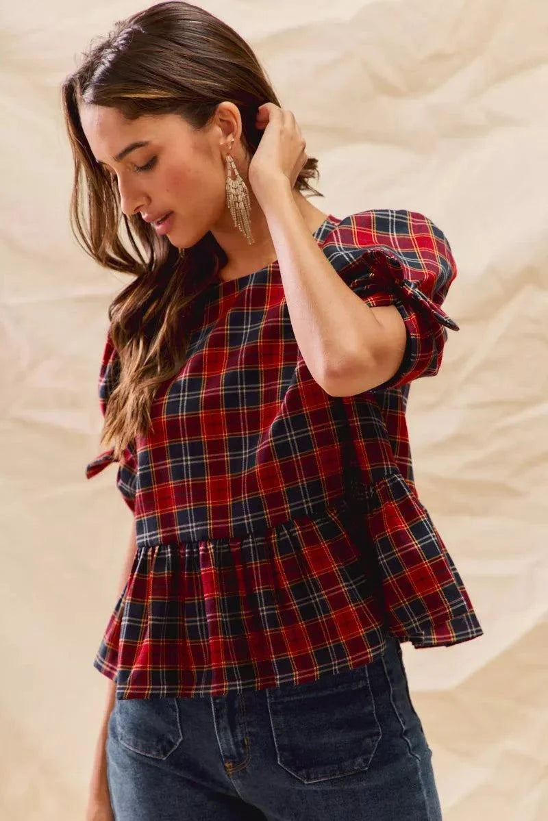 Woman wearing Christmas holiday plaid ribbon short sleeves top with ruffle and tied details, styled for festive season