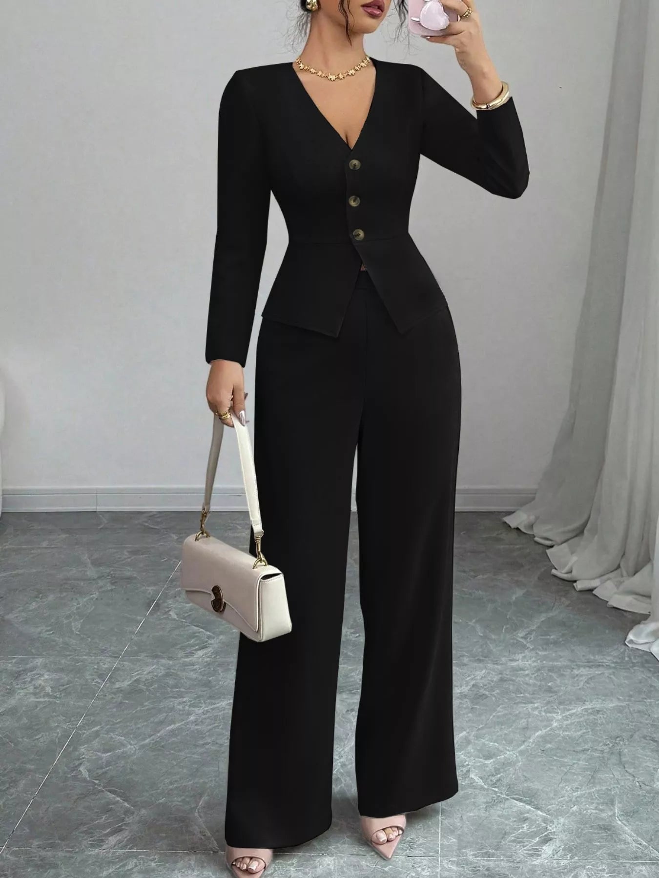 Woman wearing black button up long sleeve top and pants set with gold buttons and beige handbag