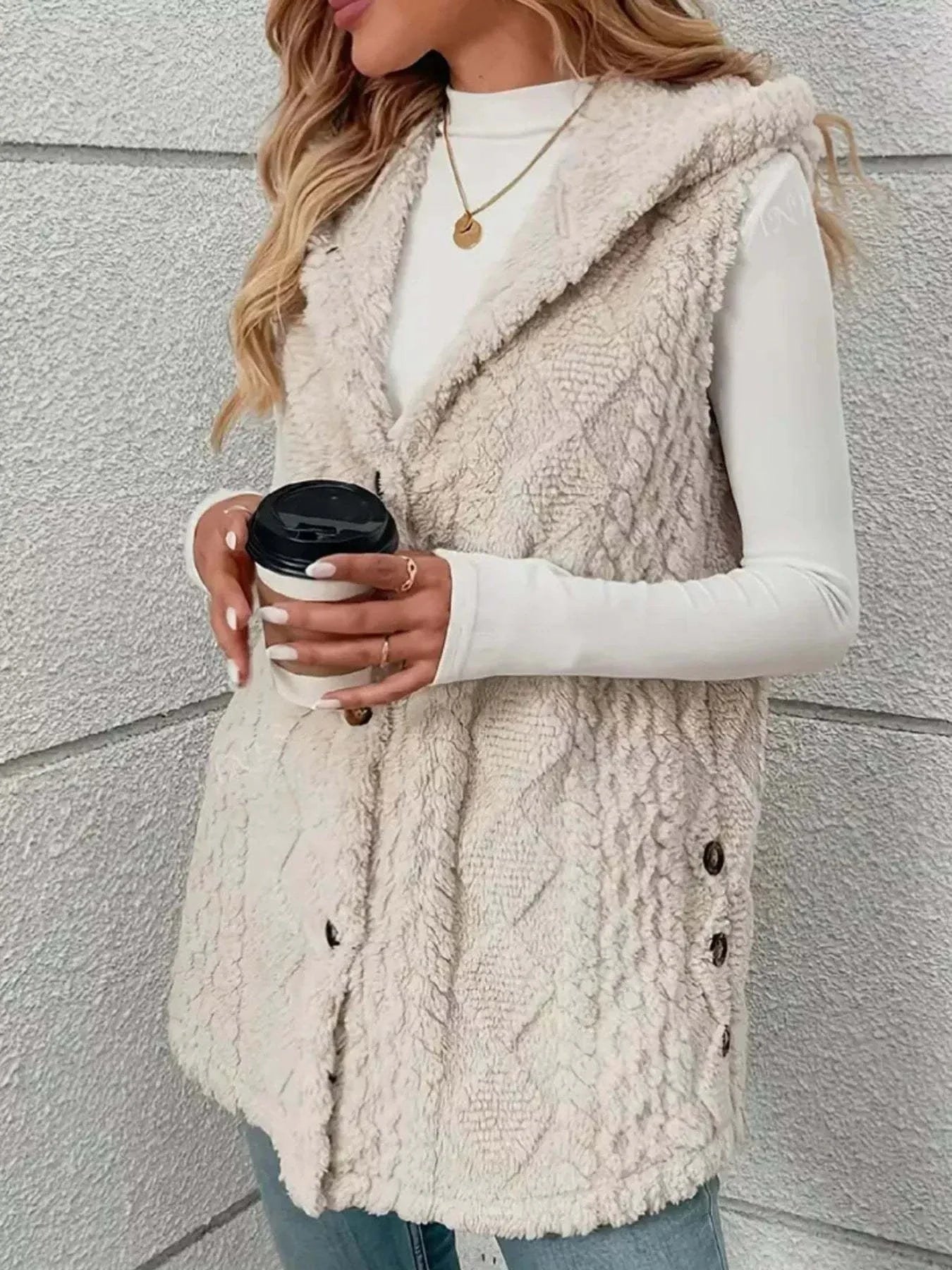 Woman wearing beige button up plush hooded vest holding coffee cup outdoors