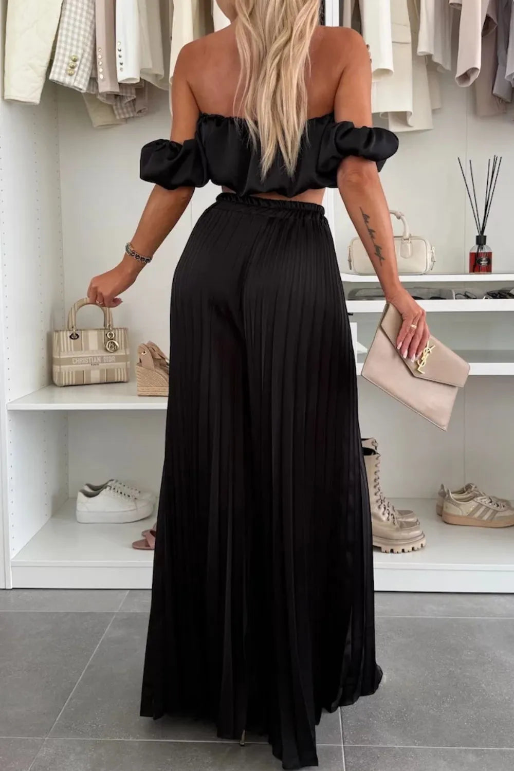 Woman wearing black off-shoulder ruffled top and pleated wide-leg pants set with clutch bag