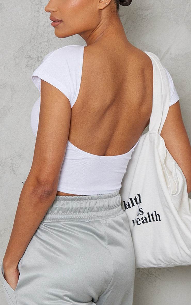 Back view of a white soft rib backless fitted short sleeve top worn with light grey pants and a white tote bag