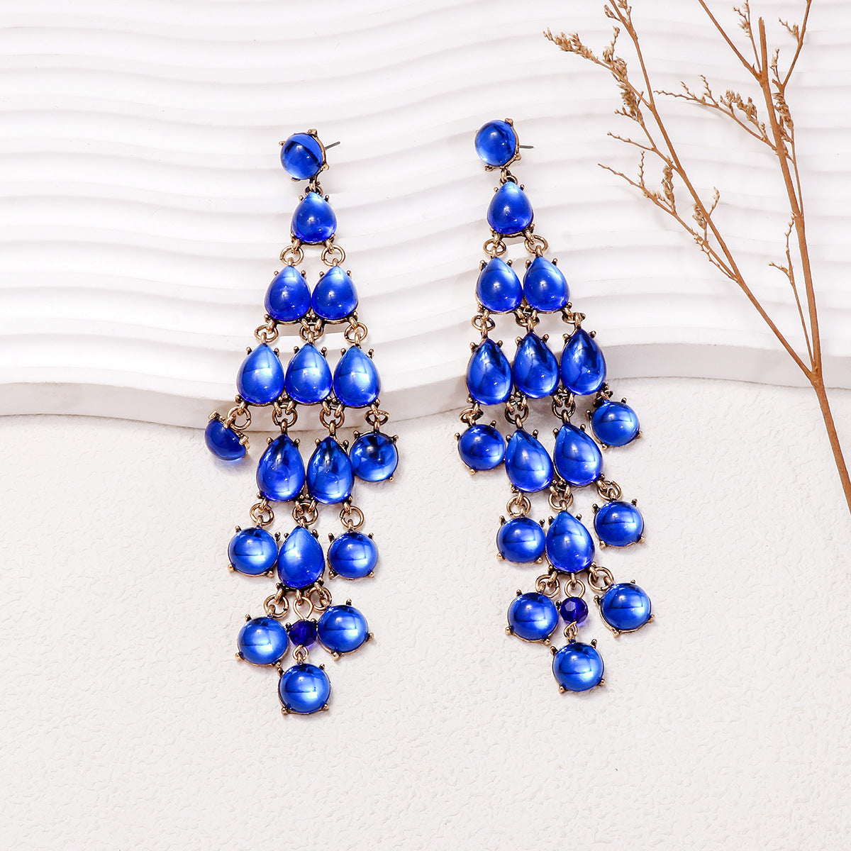 Blue alloy and rhinestone teardrop chandelier earrings on white textured surface with dried grass decoration