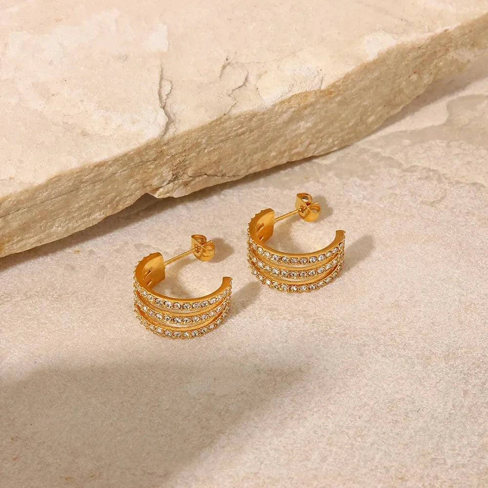 Gold-plated stainless steel C-hoop earrings with inlaid zircon stones on a beige stone surface