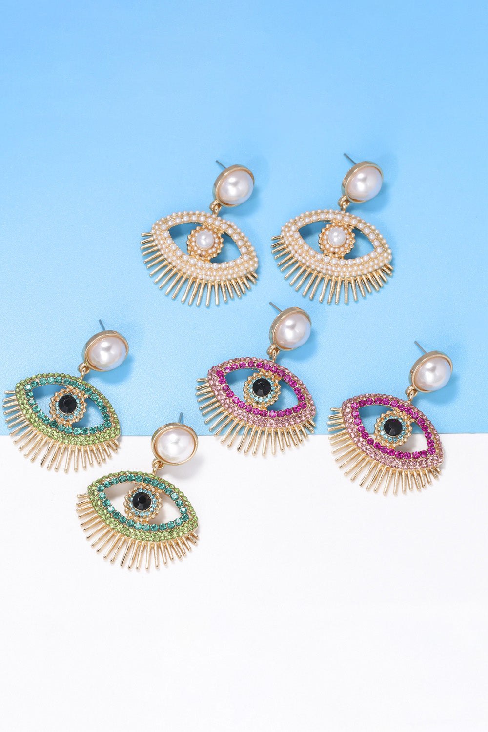 Set of modern evil eye shape rhinestone dangle earrings with synthetic pearl and zinc alloy on blue and white background
