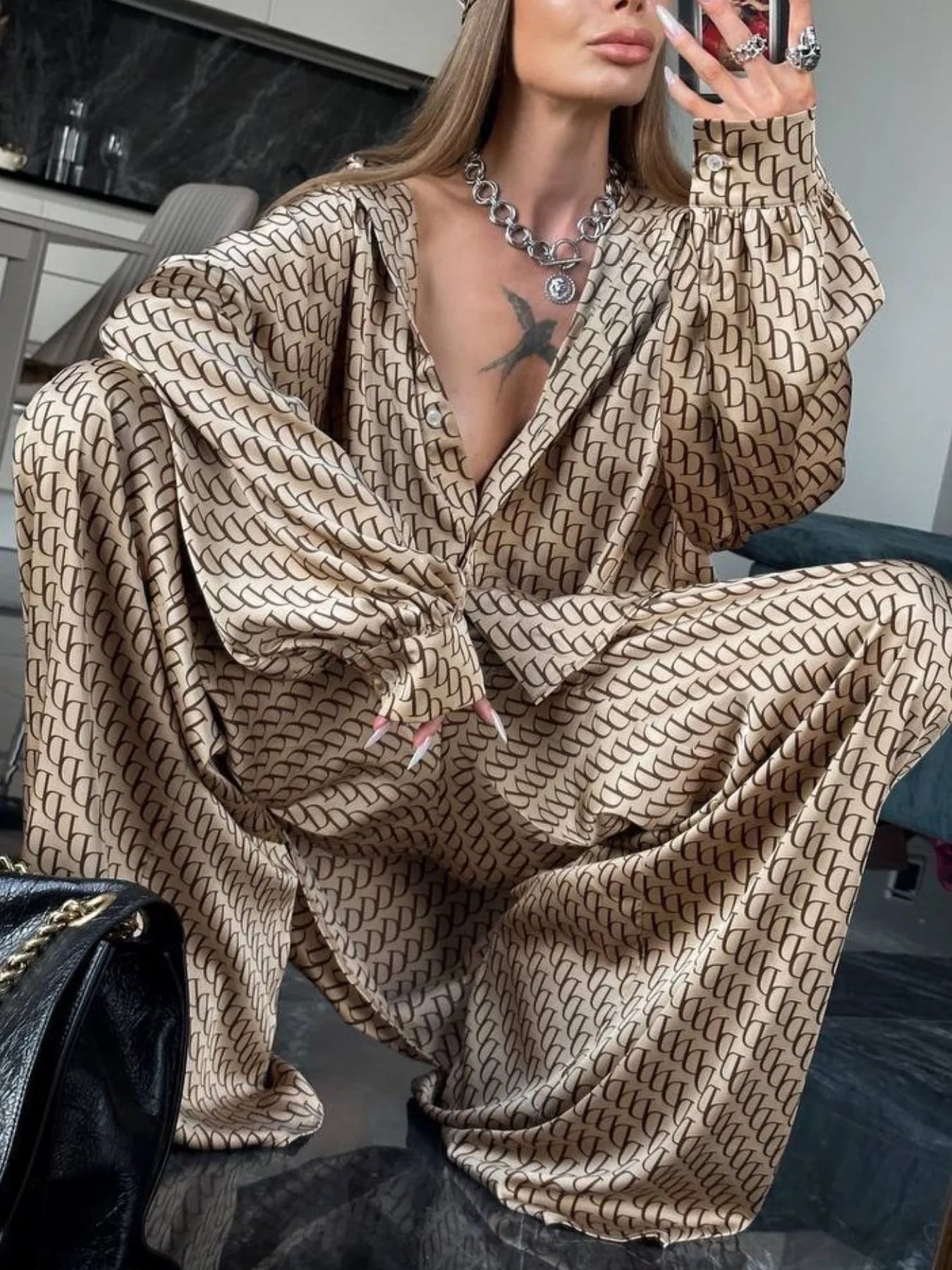 Oversized printed button up shirt and pants set in beige with black pattern, worn by a woman sitting indoors, featuring relaxed fit and 100% polyester material