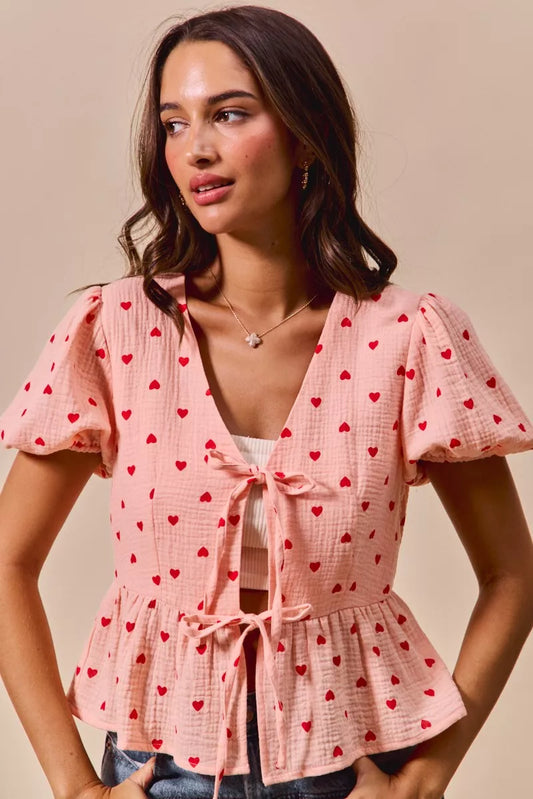 Woman wearing pink baby doll blouse with all over red hearts and ribbon tie detailing