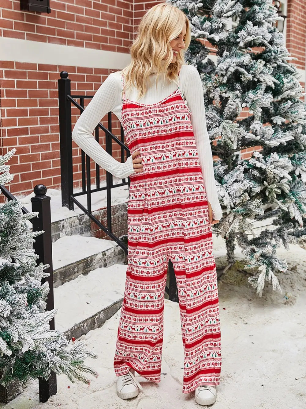 Woman wearing shiny Christmas jumpsuit with color contrast and wide-legged design standing outdoors by snowy Christmas trees