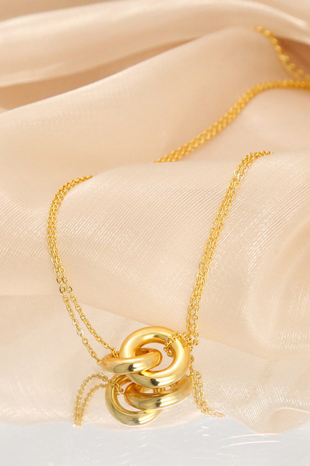 Gold linked ring pendant necklace with brass chain on beige fabric flat lay