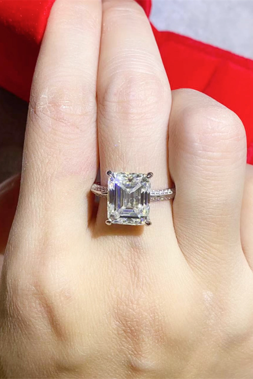5 carat moissanite platinum-plated ring on finger with emerald cut stone and sterling silver band
