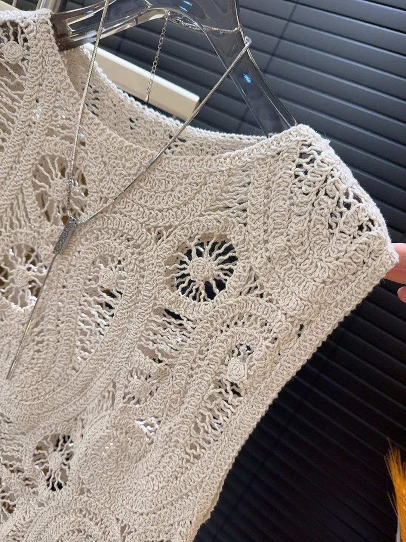 Close-up of beige crochet sleeveless tank with openwork and asymmetrical design on hanger