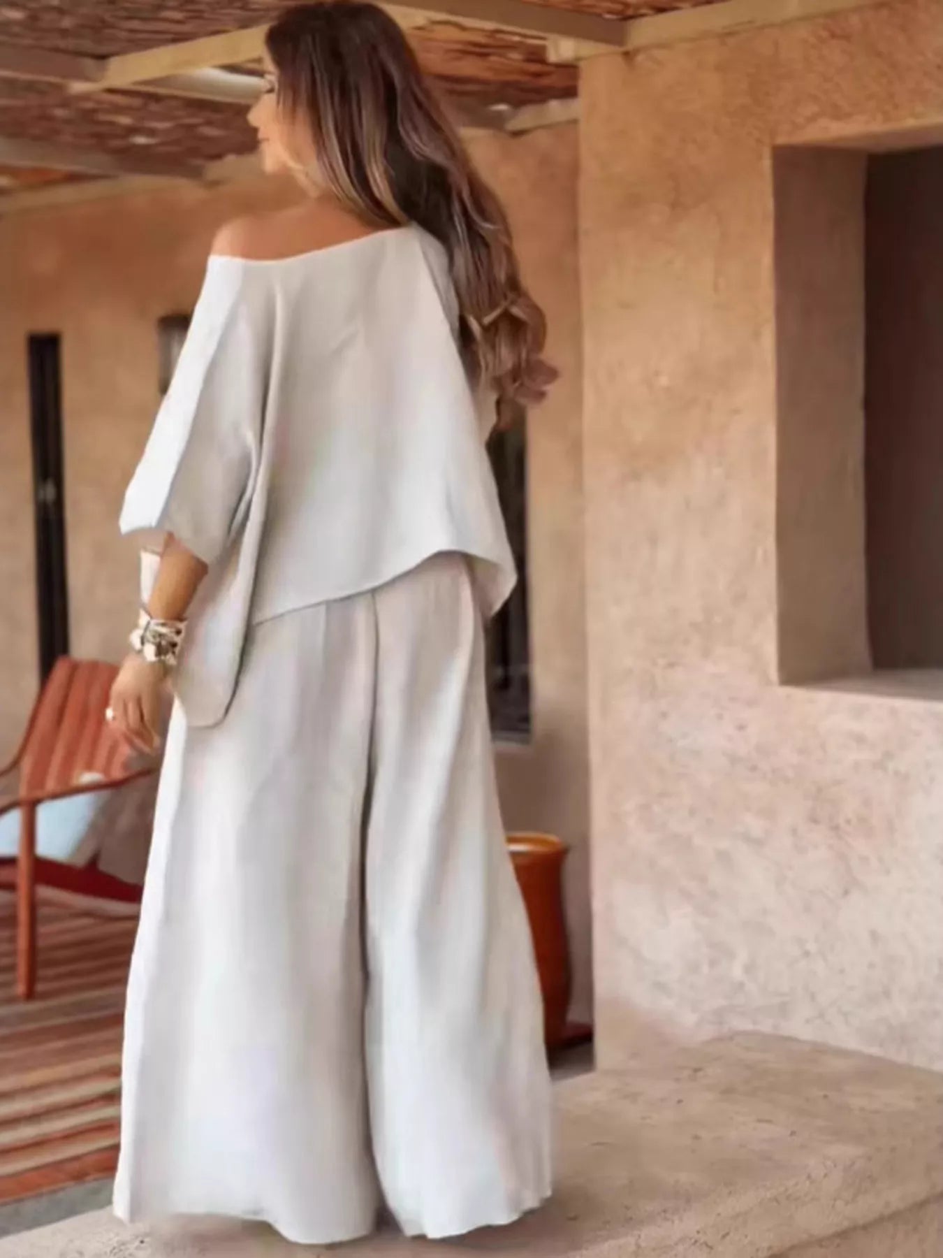 Plus size woman wearing full size boat neck top and wide leg pants set in light color from the back