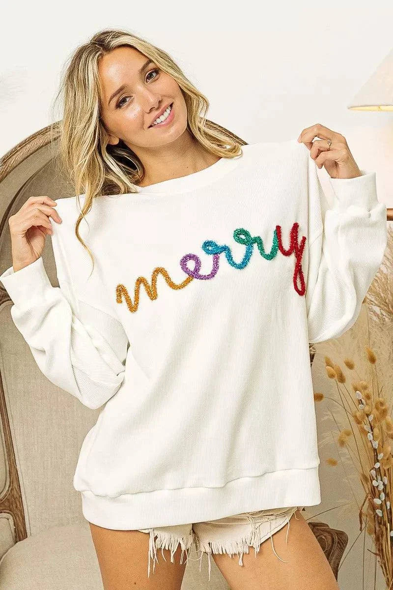 Woman wearing white drop shoulder sweatshirt with colorful Merry Tinsel Lettering on front