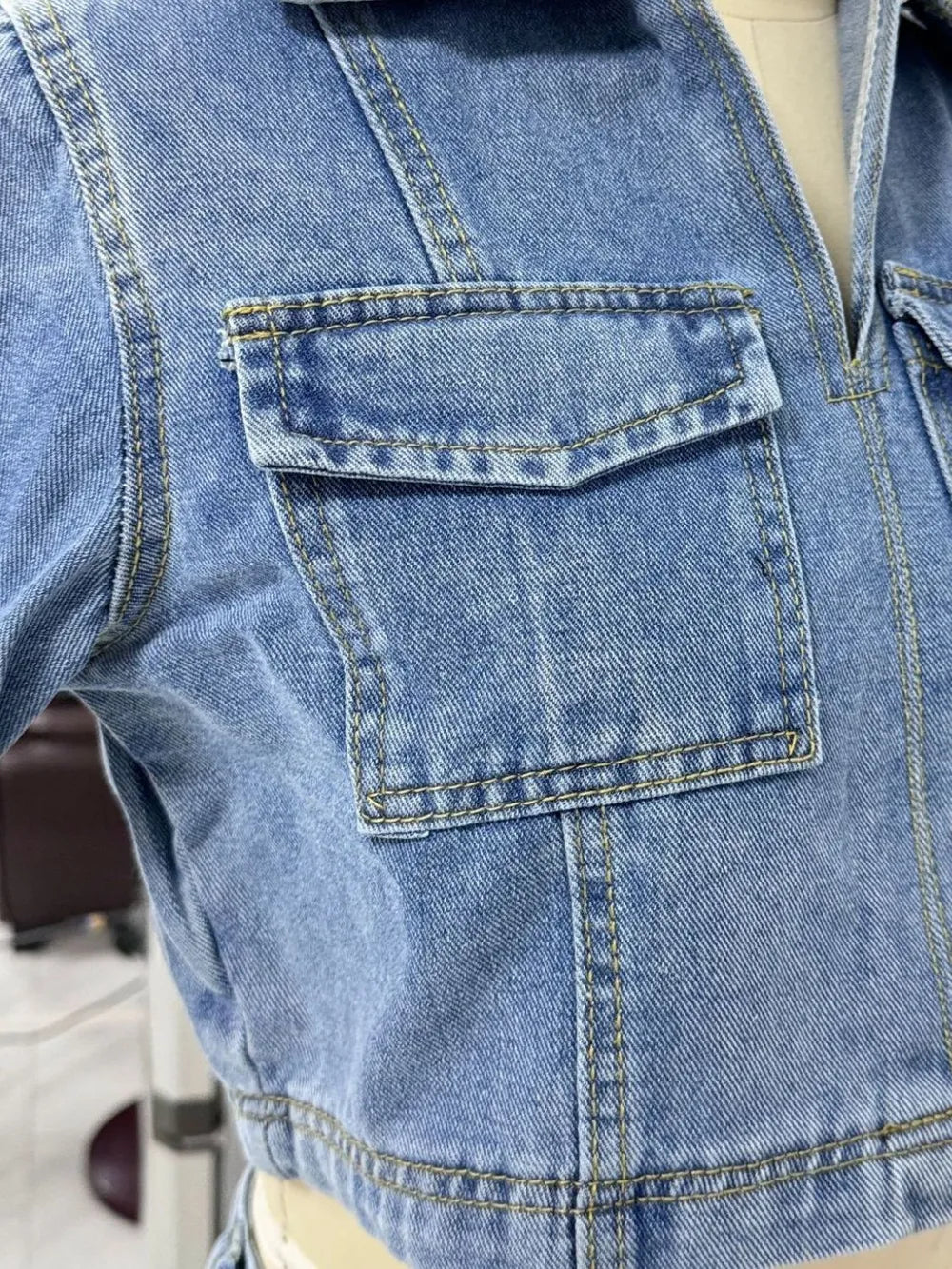 Close-up of denim Johnny Collar Short Sleeve Top pocket detail in blue fabric