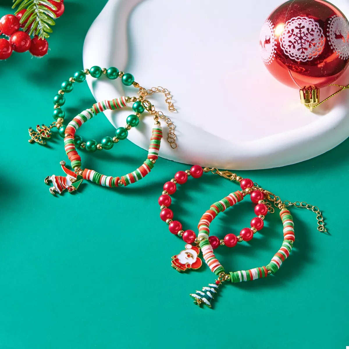 Christmas charm bracelet set with green, red, and striped beads featuring festive holiday charms on a teal background with Christmas ornament.