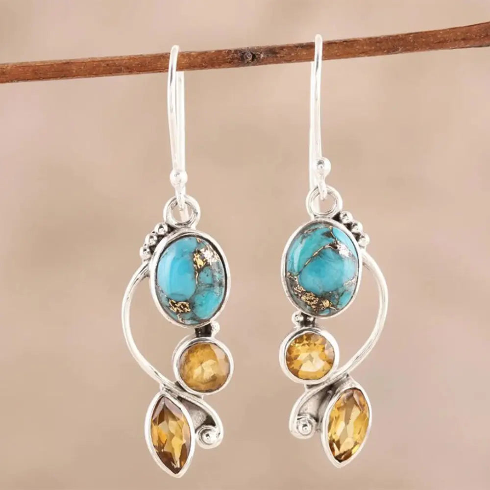 Geometric alloy dangle earrings with turquoise and amber stones hanging on a branch