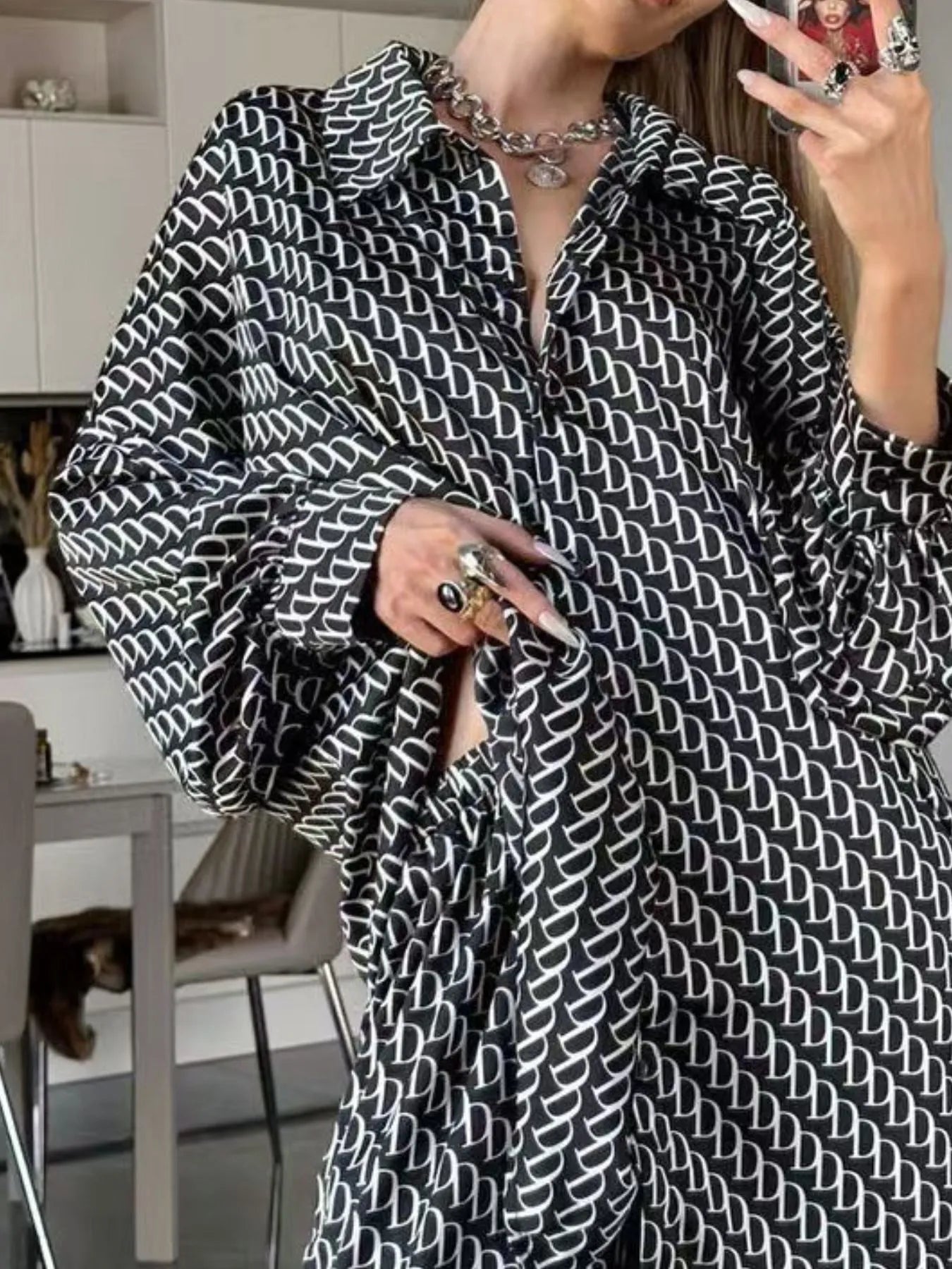 Black and white oversized printed button up shirt and pants set with chain necklace and rings in modern room interior