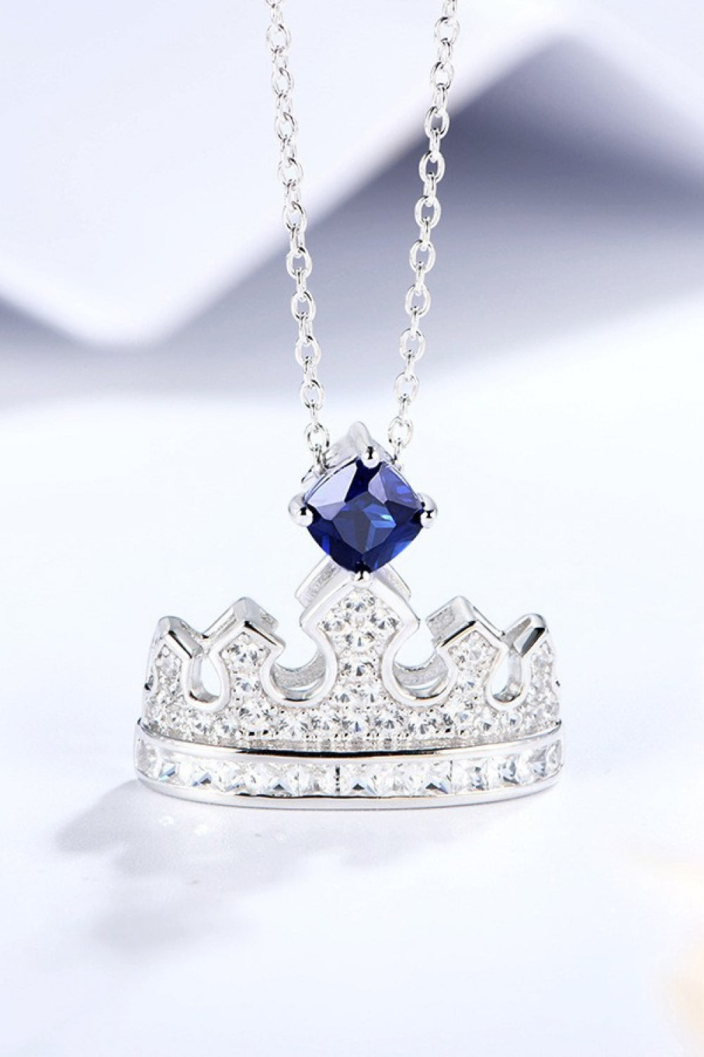 Minimalist crown-shaped pendant necklace with lab-grown sapphire and zircon in platinum-plated 925 sterling silver.