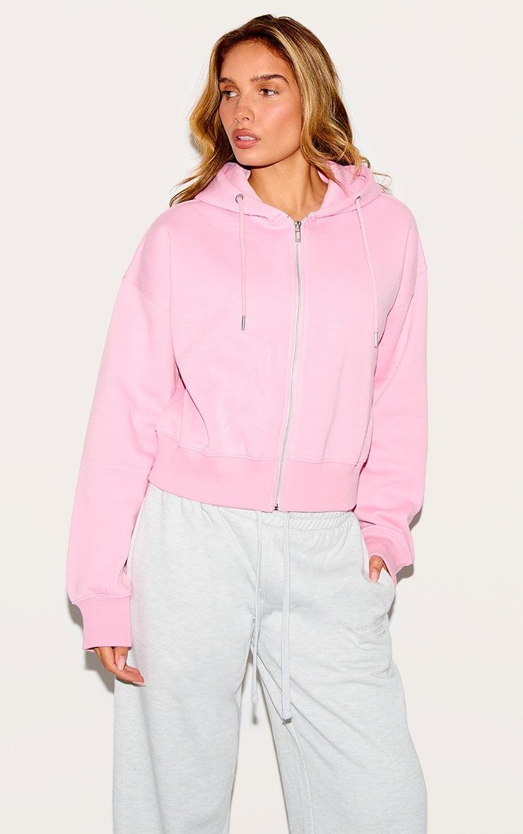 Woman wearing a bubblegum pink zip-up hoodie with "Chill Club" puff print and light gray pants