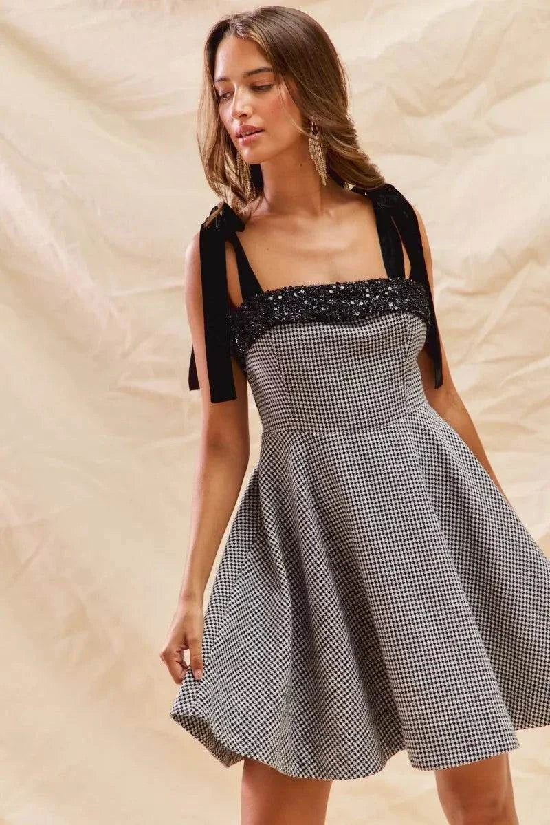 Woman wearing houndstooth fit flare mini dress with black shoulder ties and sequin trim