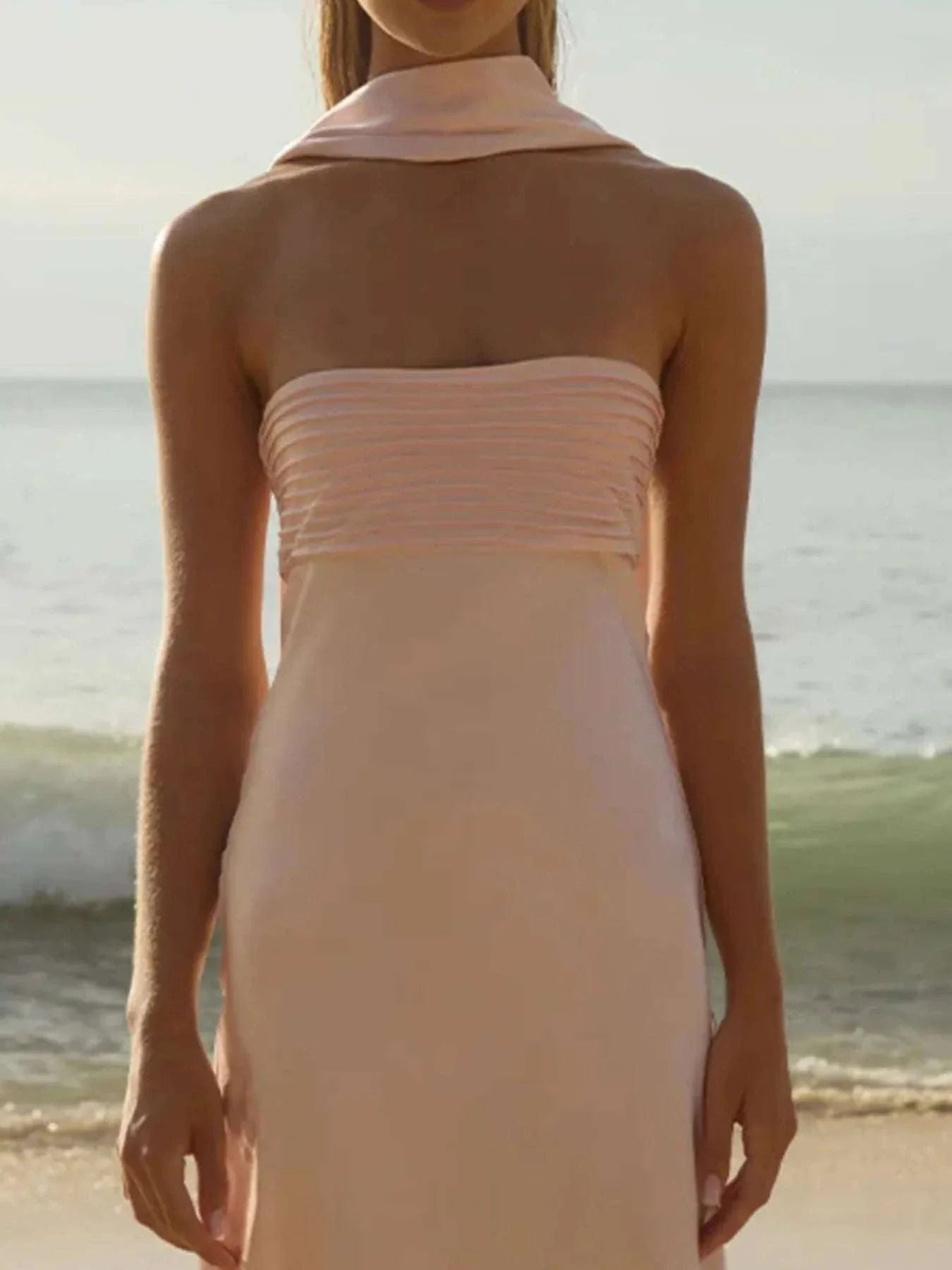 Woman wearing a pale pink tube mermaid maxi dress on the beach with no stretch and zipper detail.