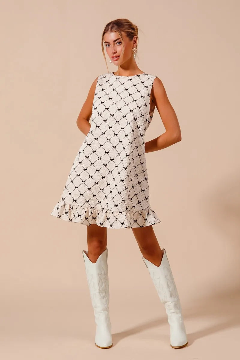 Woman wearing SO ME Texture Bow sleeveless mini dress with ruffle hem and white boots