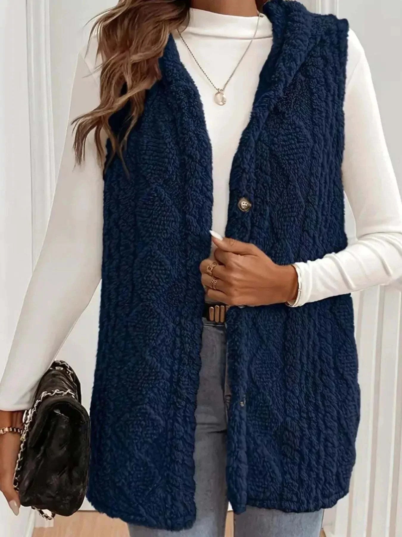 Woman wearing navy blue button up plush hooded vest with cable knit pattern over white long-sleeve top