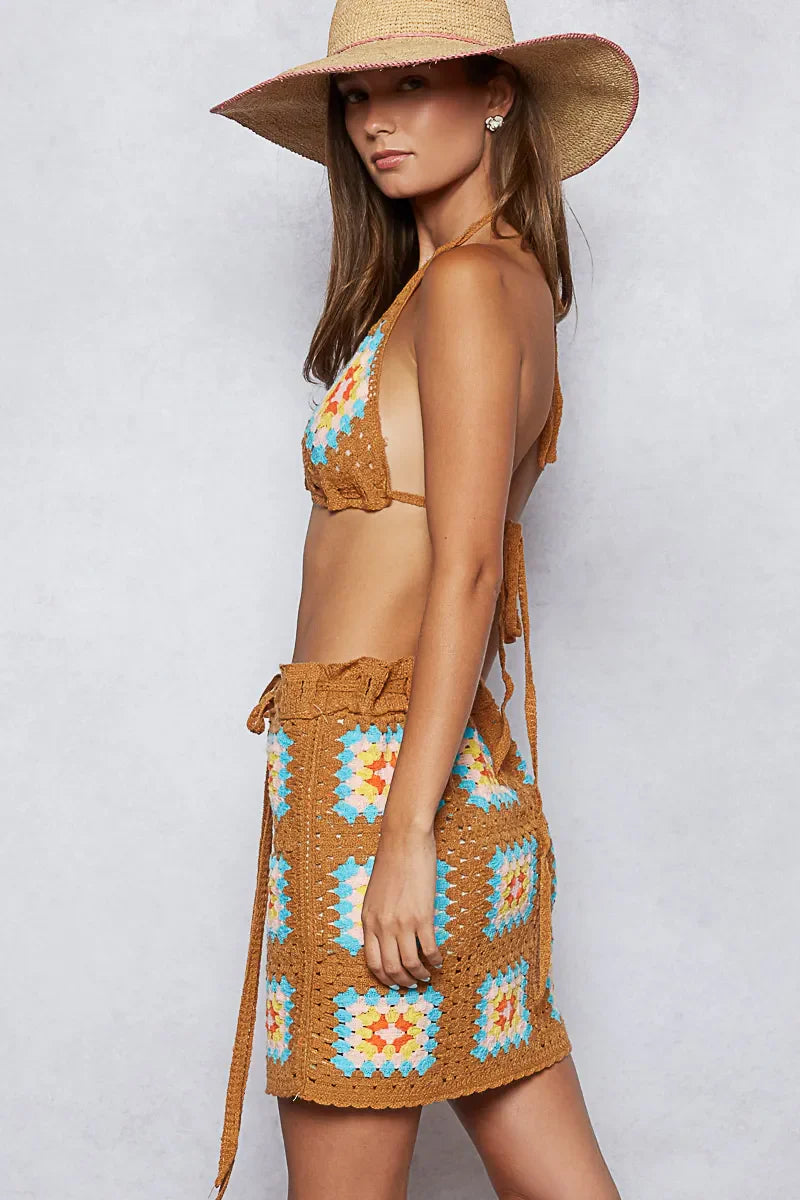 Woman wearing POL crochet halter neck cami and skirt sweater set in brown with turquoise and white granny square pattern and wide-brim straw hat