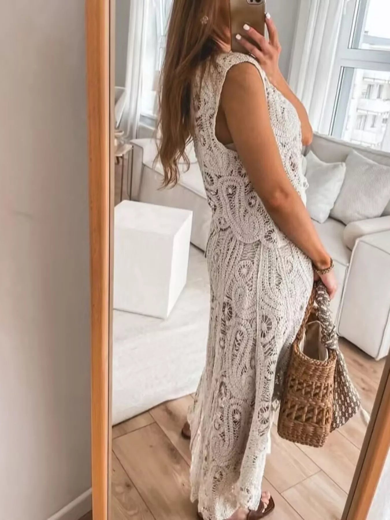 Side view of woman wearing beige crochet sleeveless tank and skirt set with openwork and asymmetrical design, holding woven handbag indoors