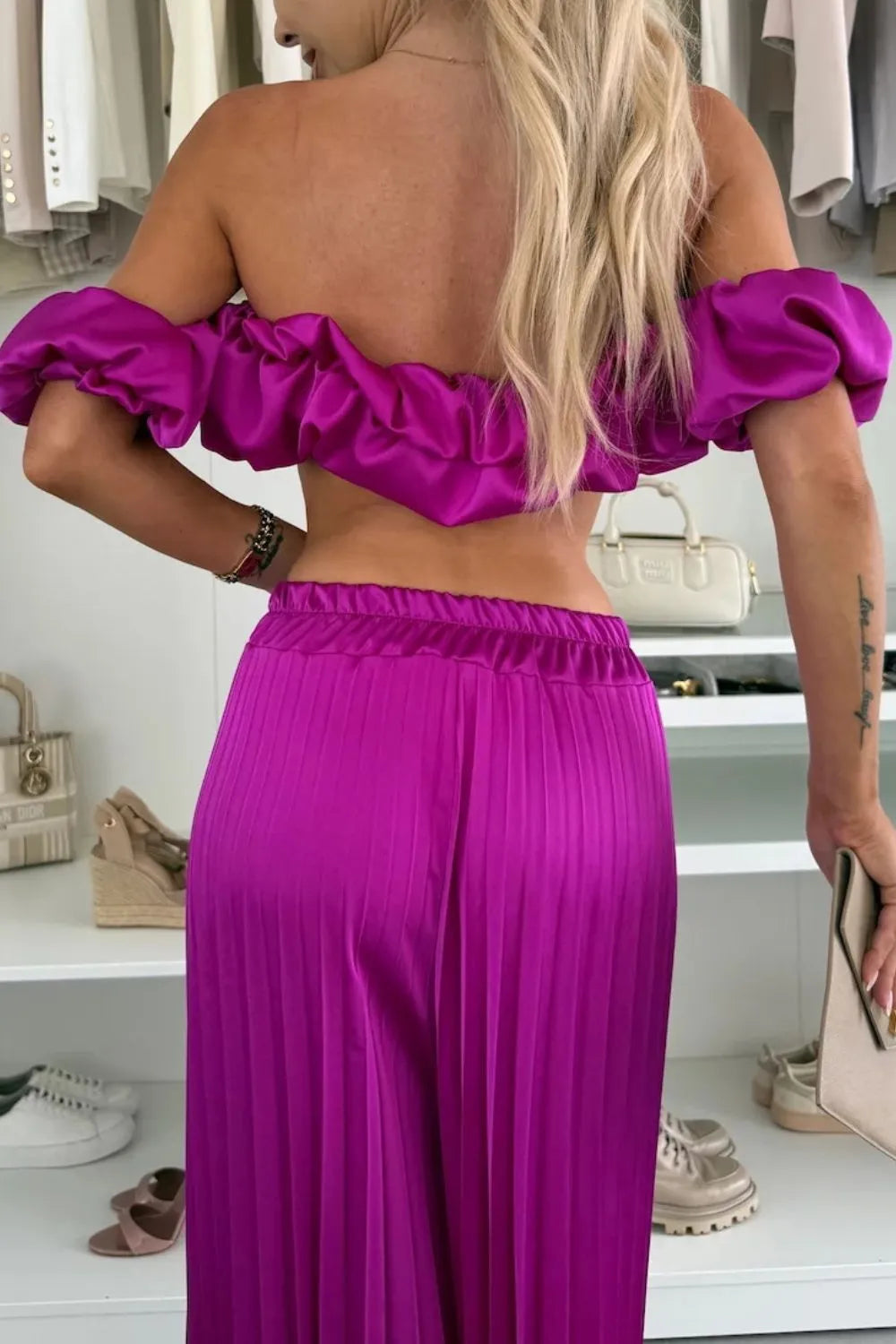 Woman wearing a vibrant purple off-shoulder ruffled top and pleated pants two-piece set