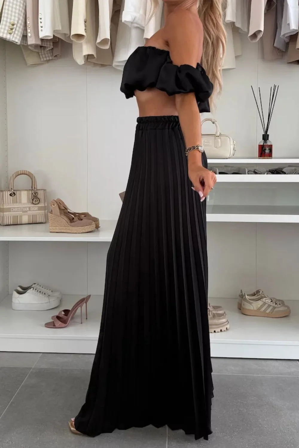 Woman wearing black off-shoulder ruffled top and pleated pants set in a modern closet room