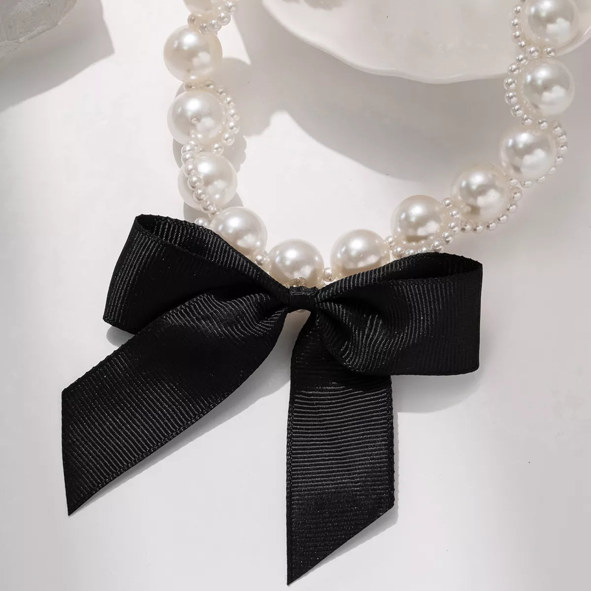 Pearl choker necklace with synthetic pearls and black bow accent on alloy chain