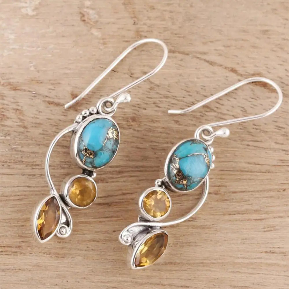 Geometric alloy dangle earrings with turquoise and amber stones on wooden background