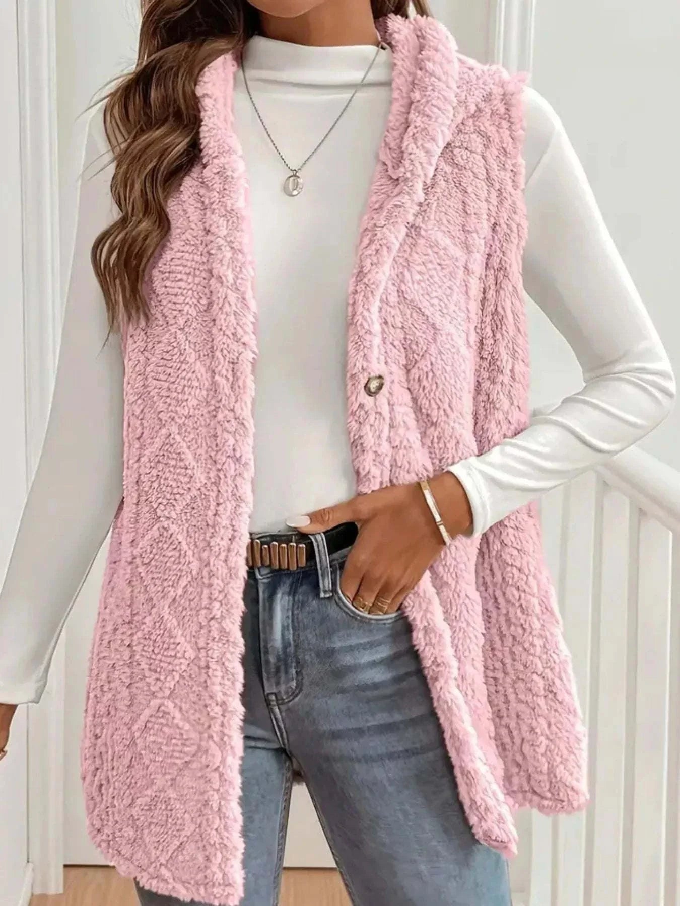 Pink button up plush hooded vest worn over white long sleeve top with jeans