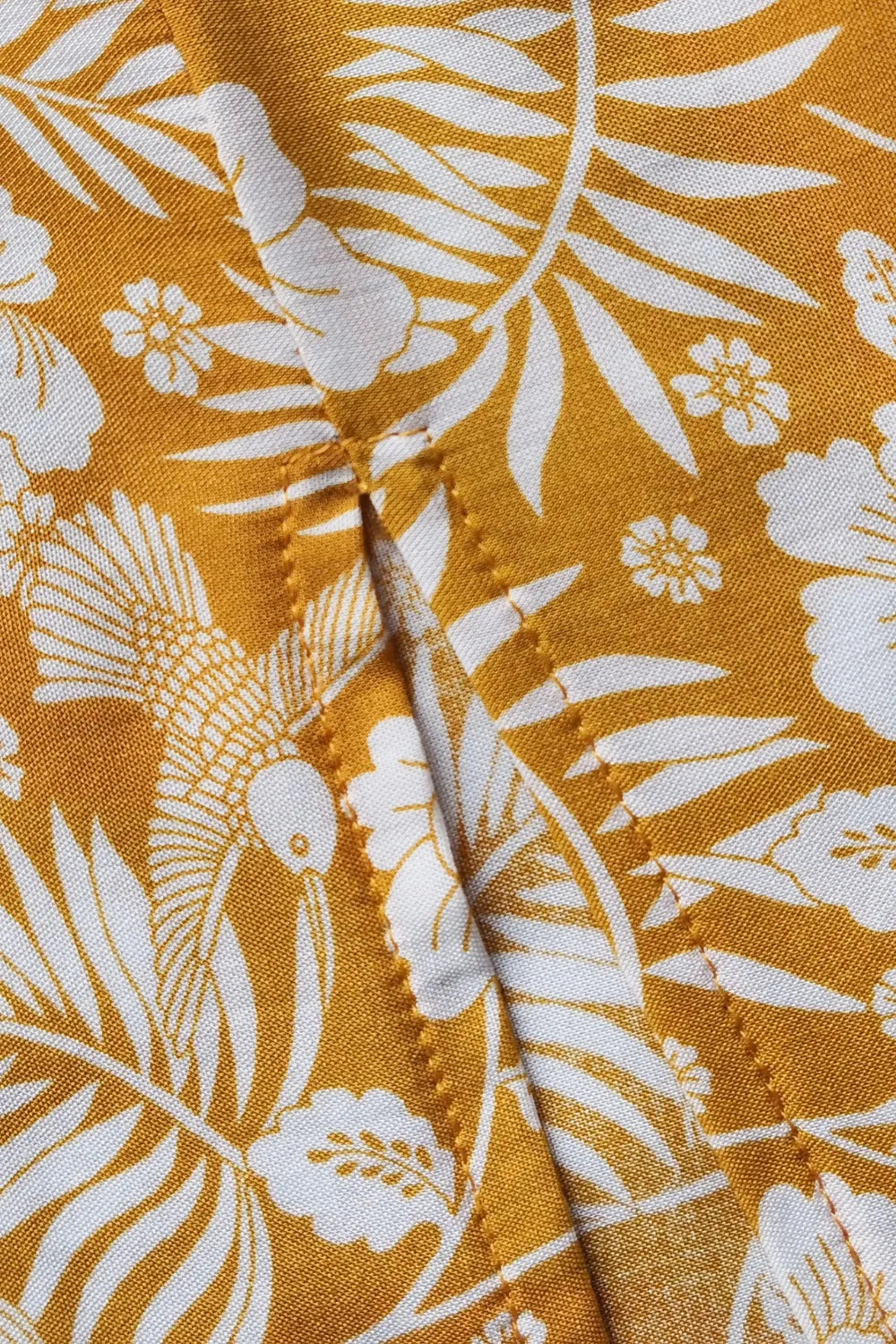 Close-up of mustard yellow printed half sleeve top with white floral and bird pattern showing slit detail