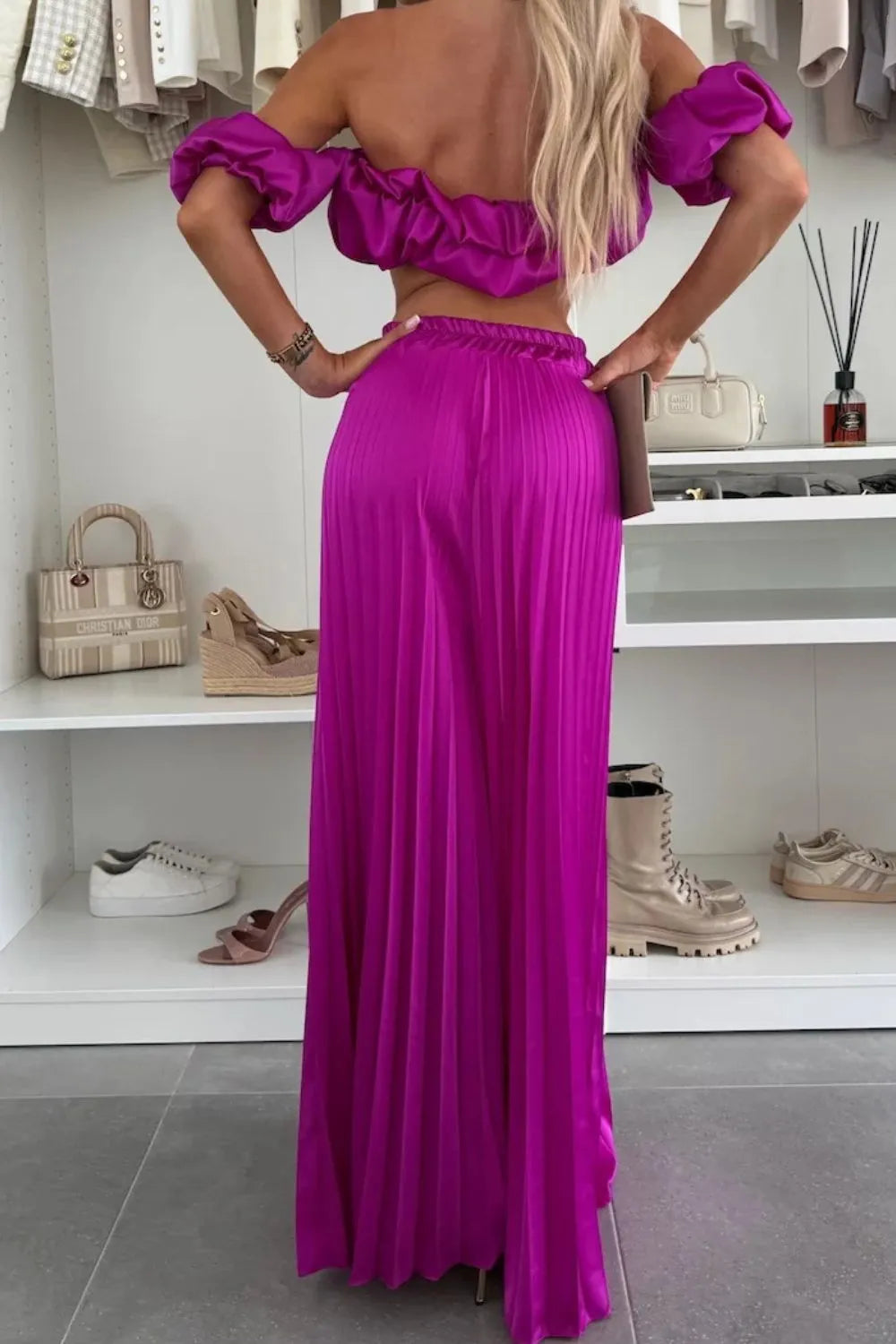 Woman wearing a vibrant purple off-shoulder ruffled top and pleated pants set, back view