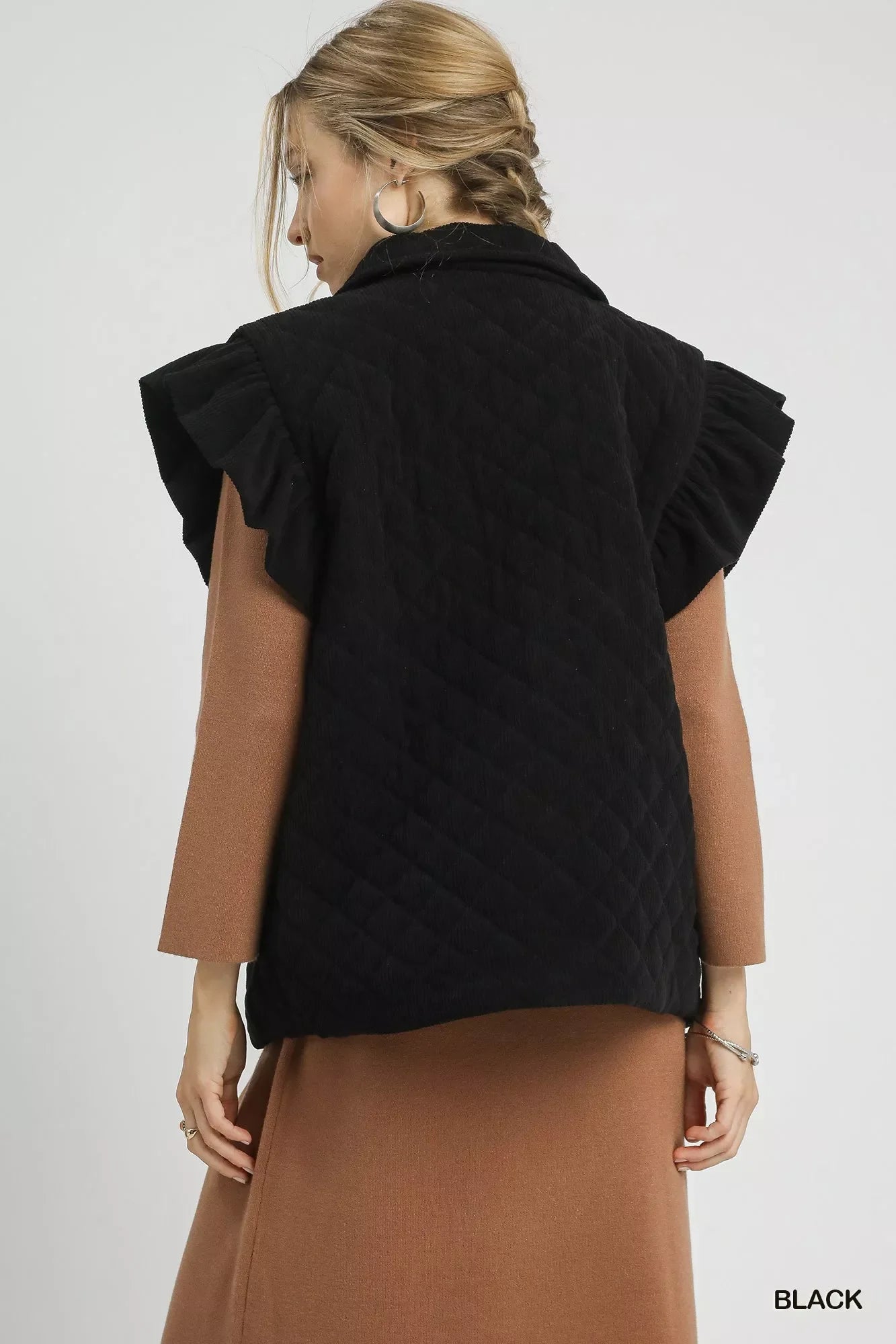 Woman wearing black Umgee Corduroy Quilted Ruffle Sleeve Vest with diamond quilt pattern and ruffle cap sleeves.