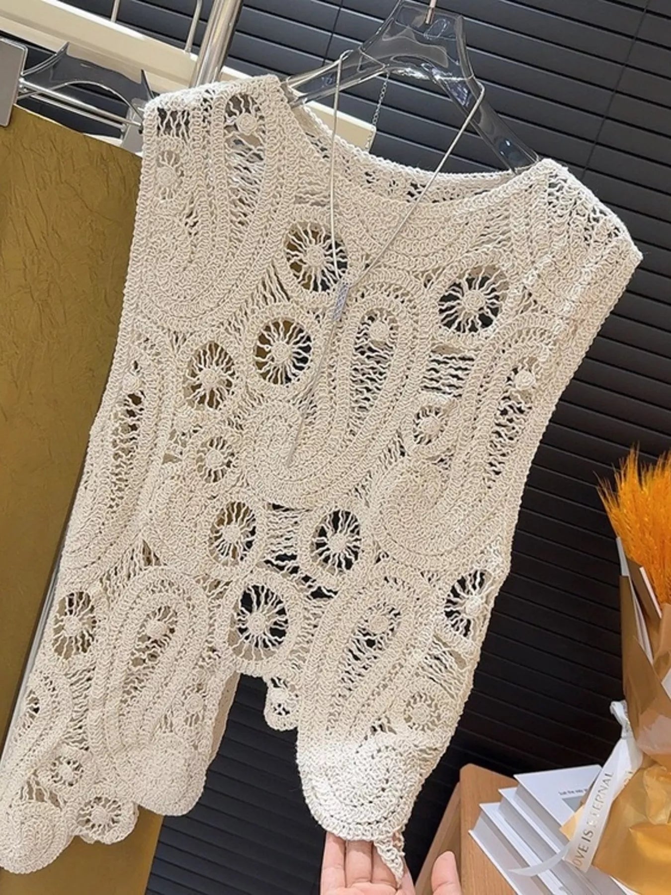 Beige crochet sleeveless tank top with openwork and asymmetrical design hanging on hanger