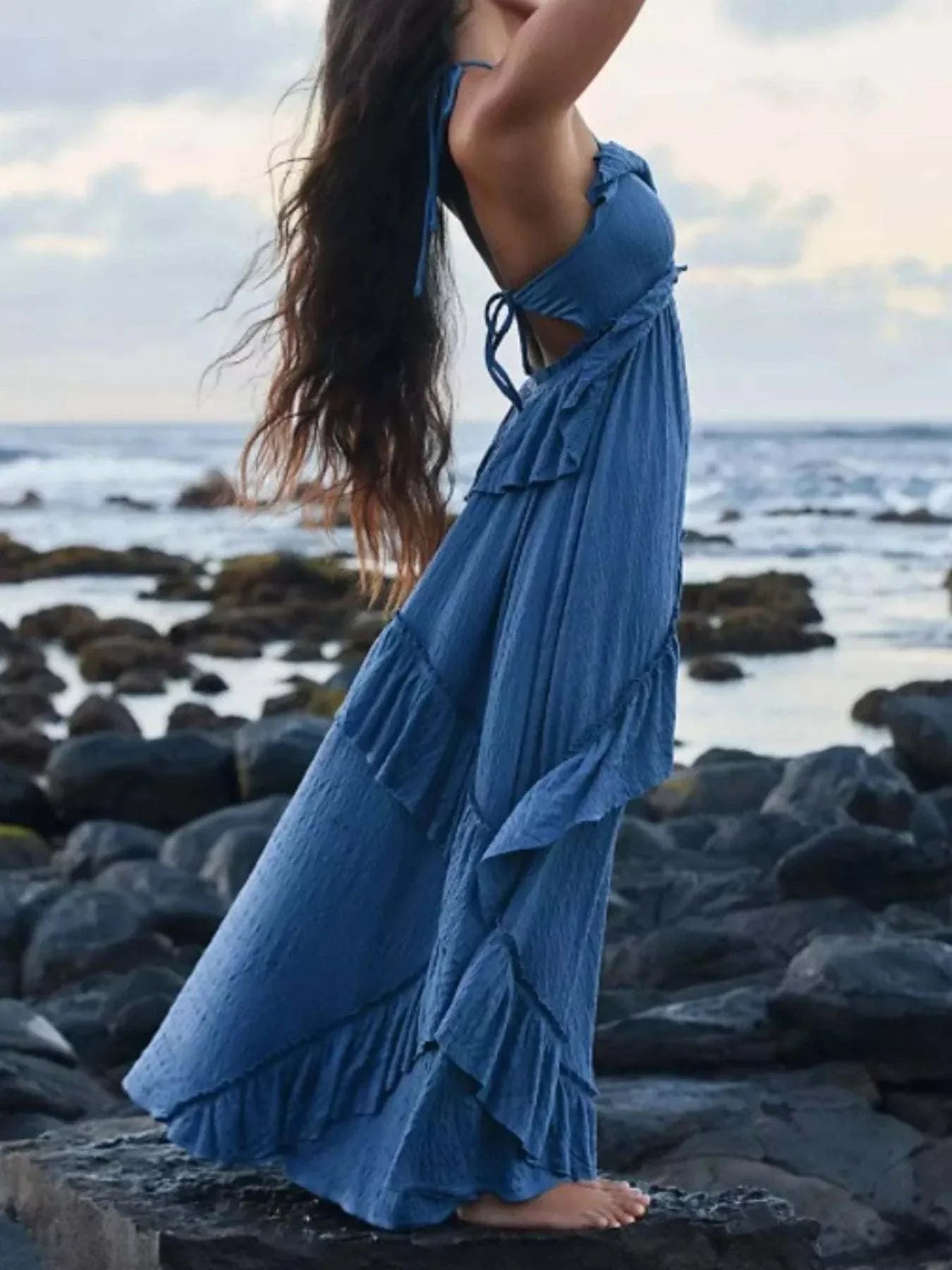 blue ruffled halter neck maxi dress with tied back, sleeveless, flowing polyester fabric by the rocky shore