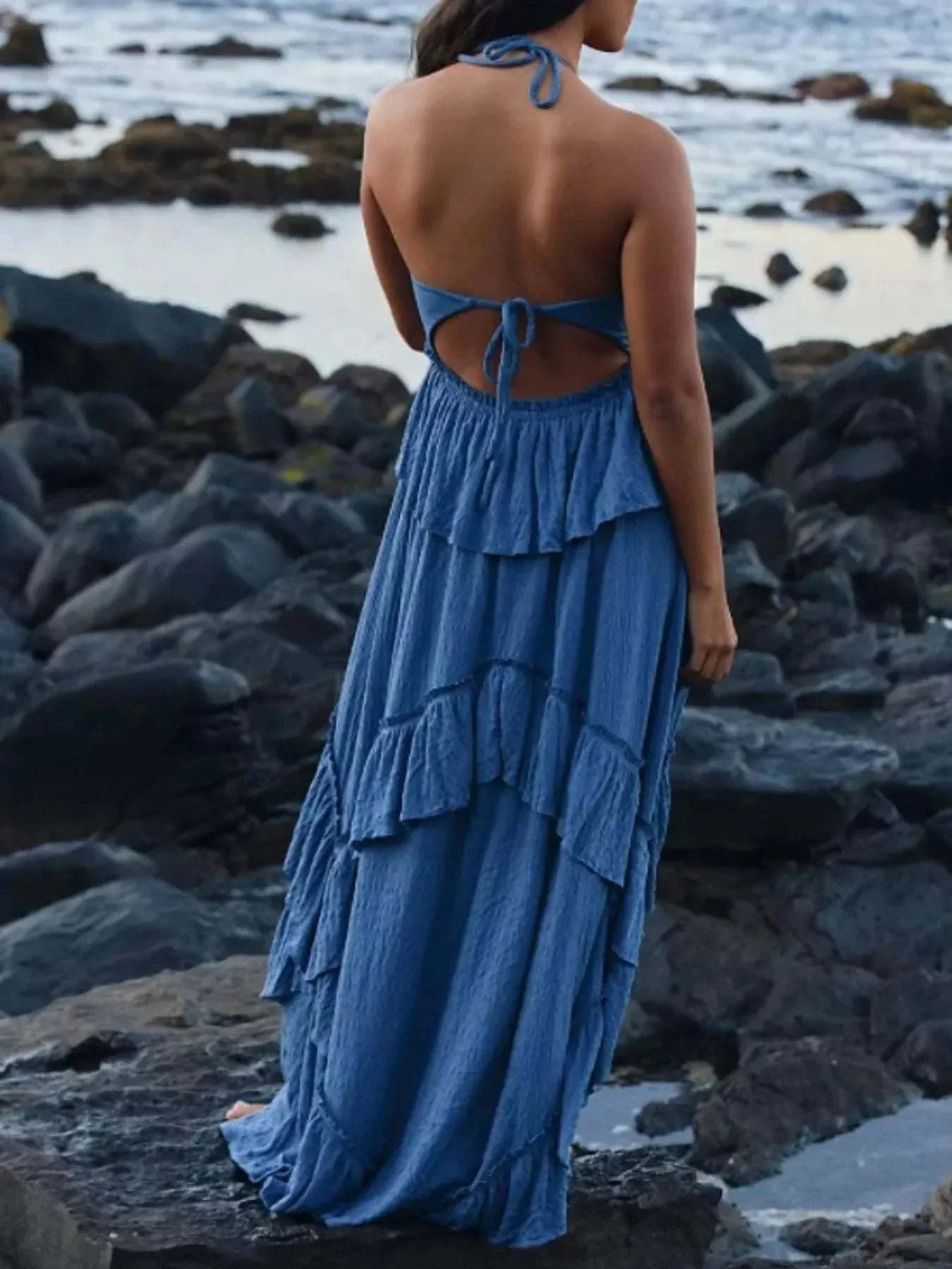 blue ruffled halter neck maxi dress back view with ties and tiered layers on rocky shore
