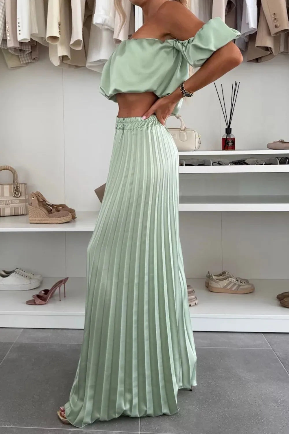 Woman wearing a mint green off-shoulder ruffled top with matching pleated pants set in a modern room