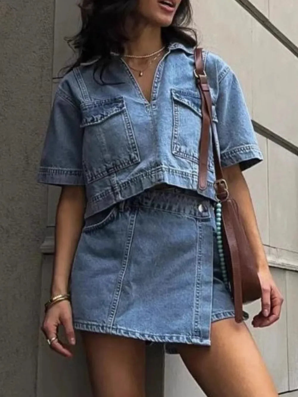 woman wearing a buttoned denim Johnny Collar short sleeve top and matching skort set with pockets and a brown shoulder bag