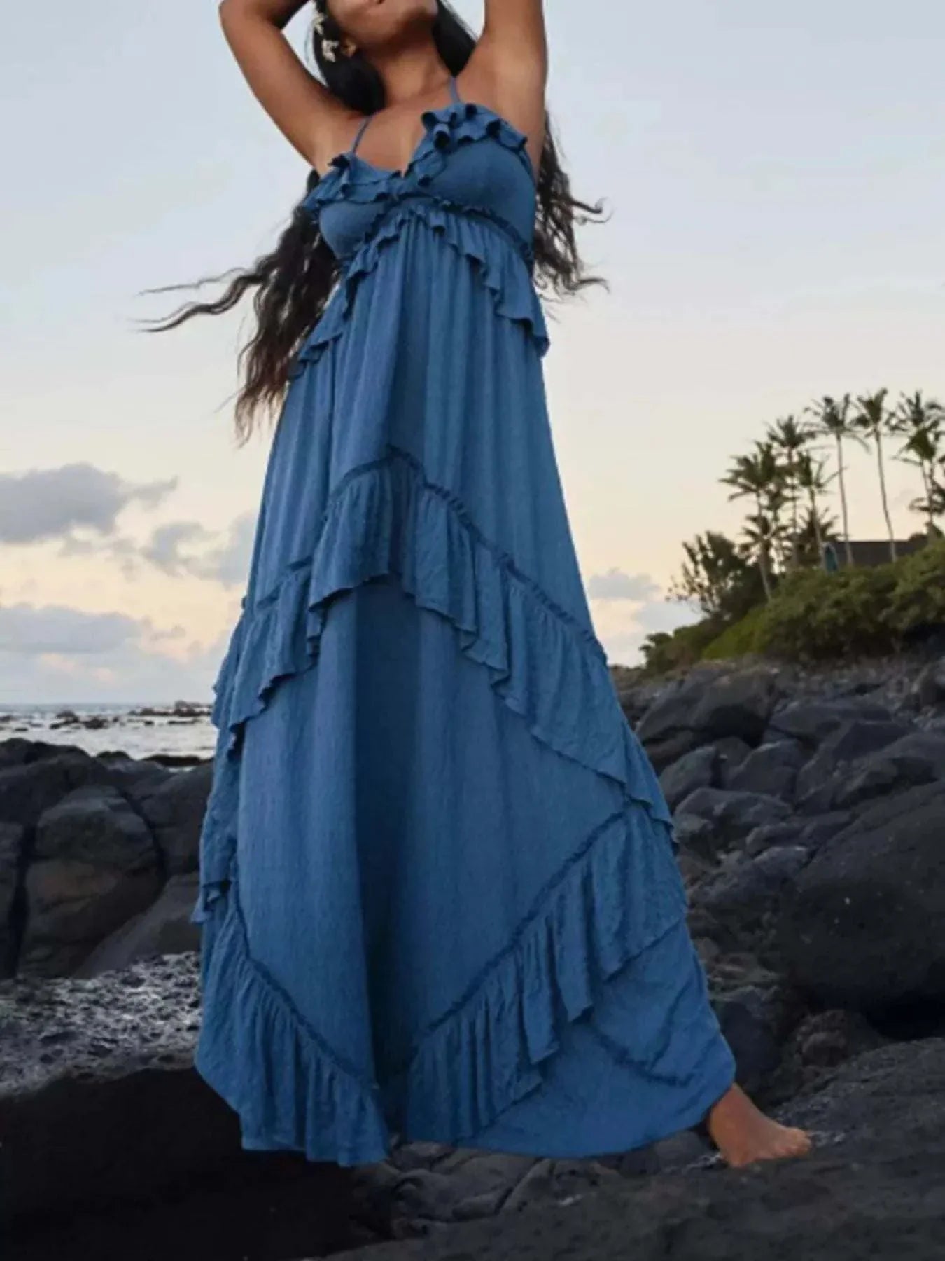 Blue ruffled halter neck maxi dress with layered ruffle details by the rocky beach